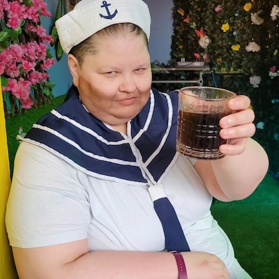 Sandy Bawls, holding a glass of rum and smirking at the camera